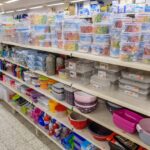 Regal in einem Geschäft mit verschiedenen Plastikbehältern, Schüsseln und Küchenutensilien.