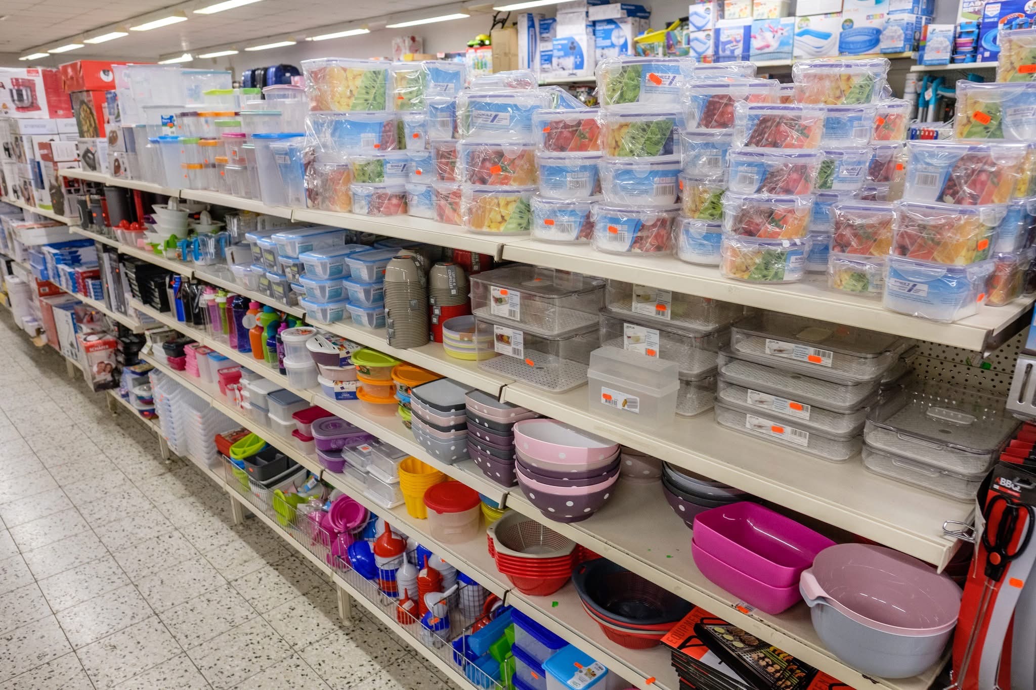 Regal in einem Geschäft mit verschiedenen Plastikbehältern, Schüsseln und Küchenutensilien.