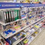 Regalwand in einem Geschäft mit verschiedenen Schreibwaren wie Ordnern, Stiften und Papeterie.