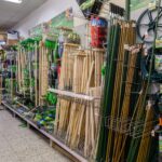 Regalwand in einem Gartencenter mit verschiedenen Spaten, Rechen, langen Holzstäben und Drahtspulen.