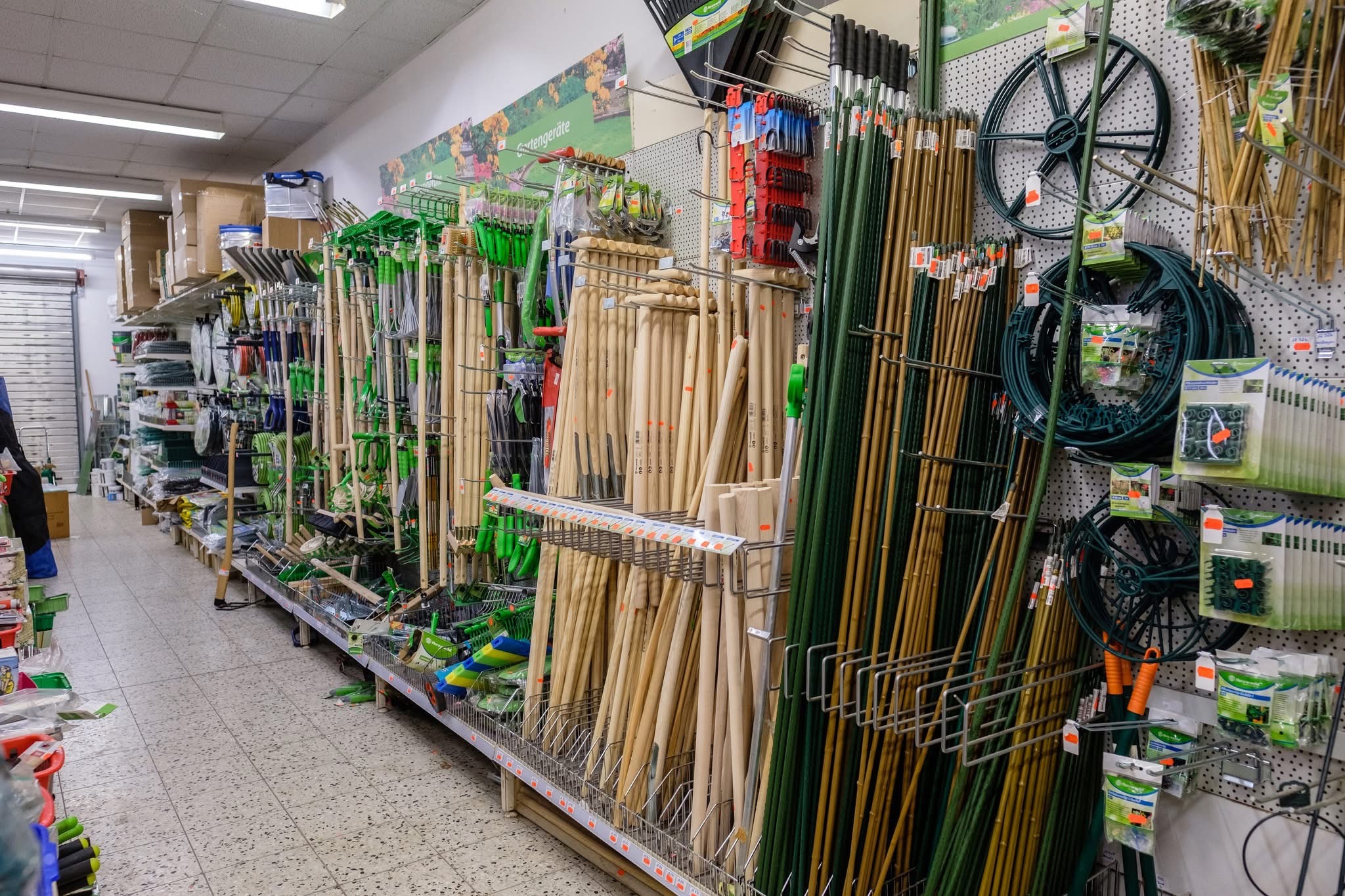 Regalwand in einem Gartencenter mit verschiedenen Spaten, Rechen, langen Holzstäben und Drahtspulen.
